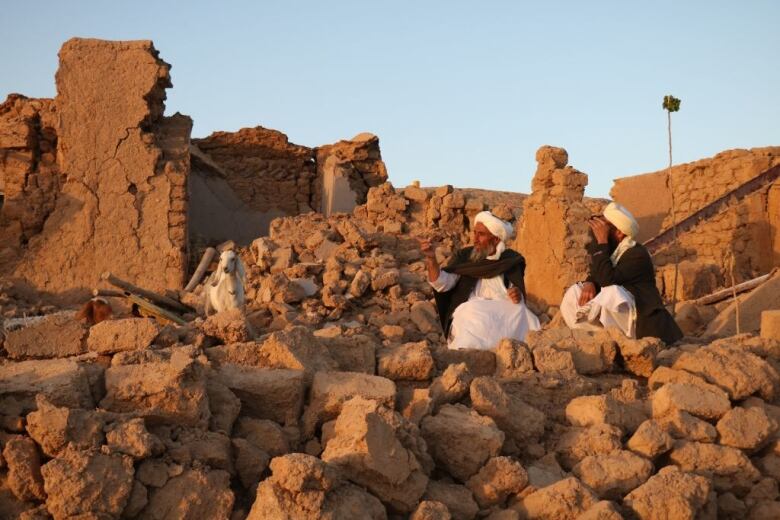 Two men sit in the rubble of an earthquake in Afghanistan.