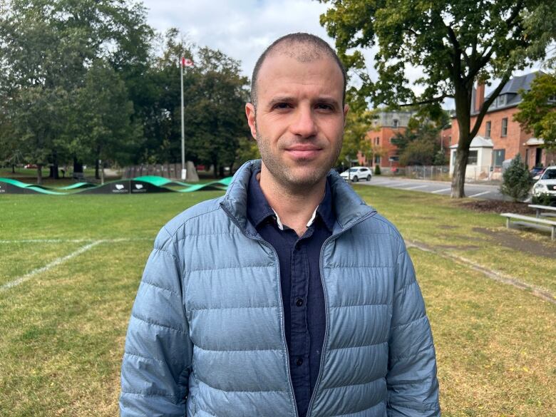 A man in blue wind breaker poses for the camera. He's standing in a soccer field. 