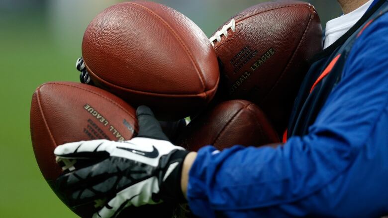 The pictures shows detail of an official holding four footballs. 