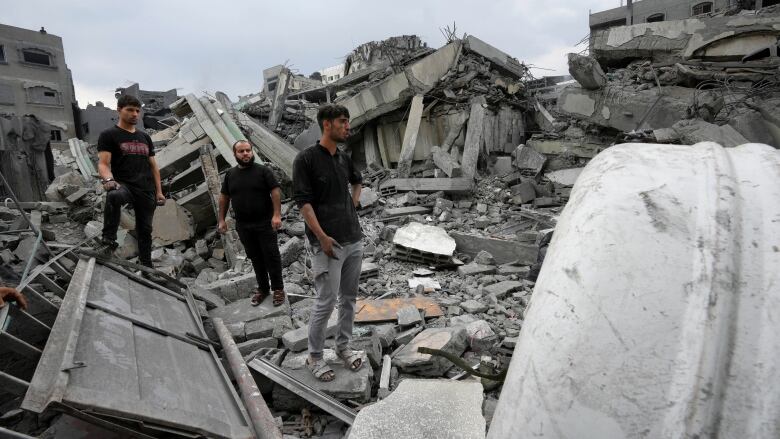 Three men wearing black clothing inspect rubble of a mosque destroyed by an airstrike.