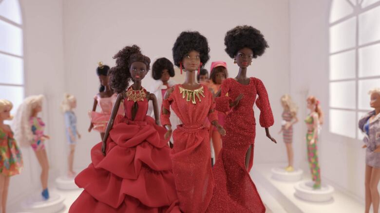 Eight Black Barbie dolls dressed in red and pink dresses appear to walk a fashion show runway. That is lined with white Barbie's on the side.