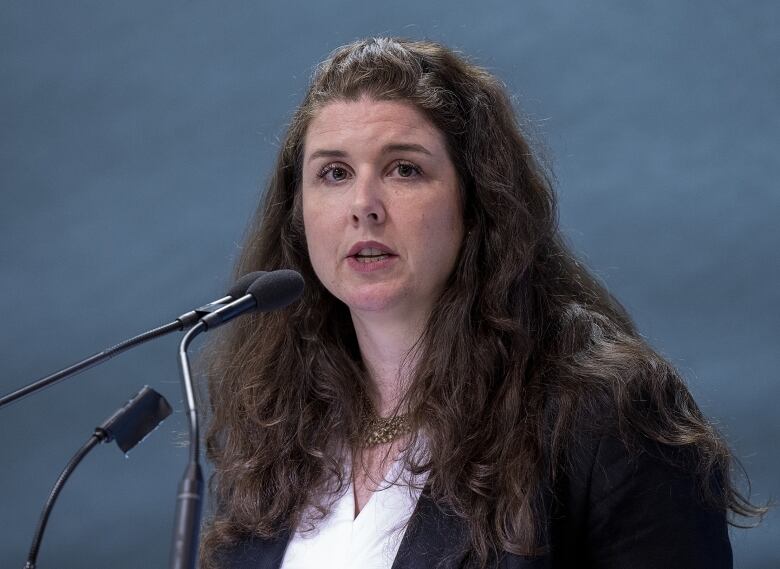 A woman stands in front of two microphones. 