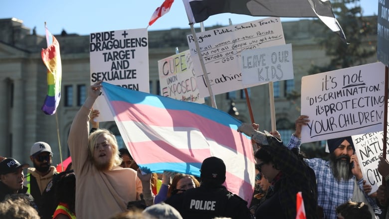 A police officer speaks with people holding a transgender flag in front of protestors in favour of the Saskatchewan government's pronoun policy. 