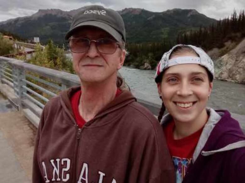 An older man and a young woman stand on a walkway alongside a river.