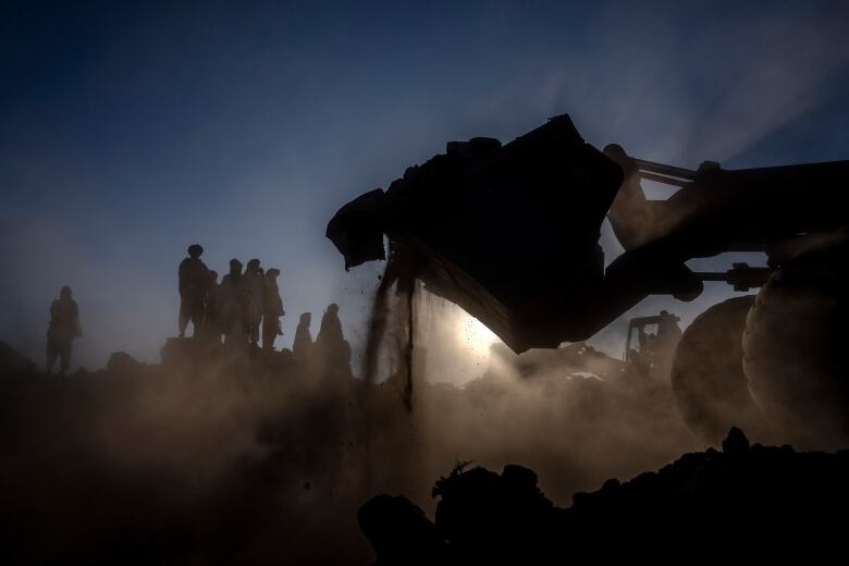 Two front-end loaders and a group of men are silhouetted against the sun.