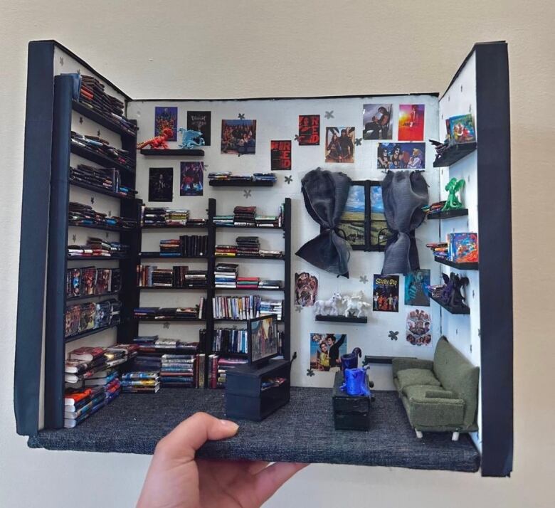 Another handcrafted miniature space, this one showing a couch and coffee table and television set. The walls are covered in bookshelves and tons of small paintings and pictures.