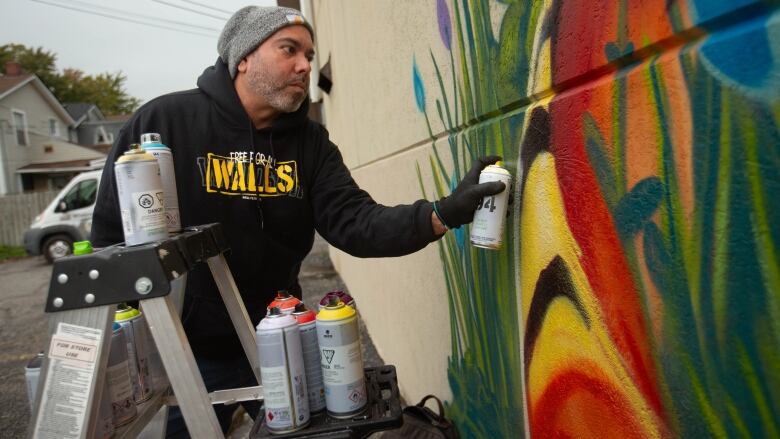 A man spray paints the side of a building in bright colours