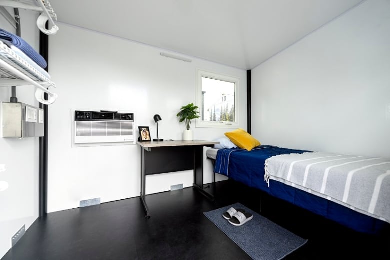 A single bed against a wall under a window and near an air conditioning unit.