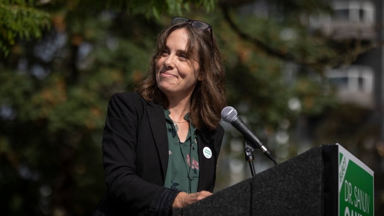 A woman speaks at a podium while wearing green.