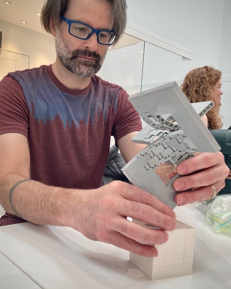 A man wearing a T-shirt holds a small, gray Lego structure.