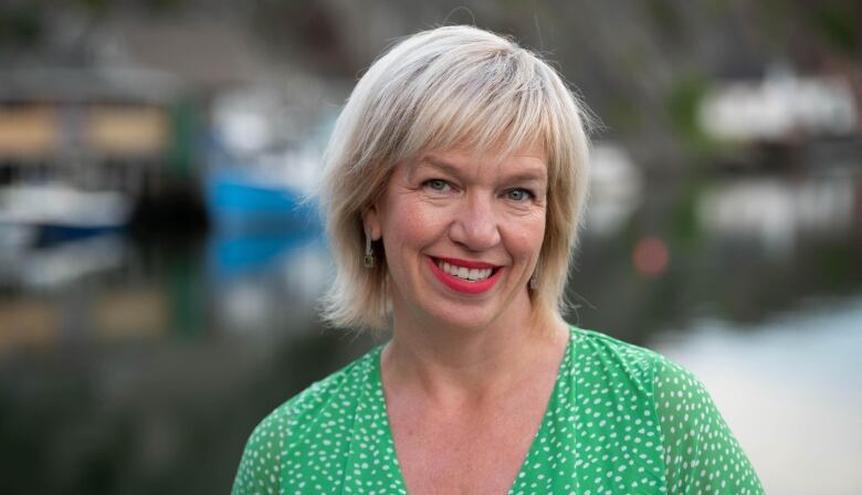 A smiling woman with short, blond hair in a green dress with small white dots.