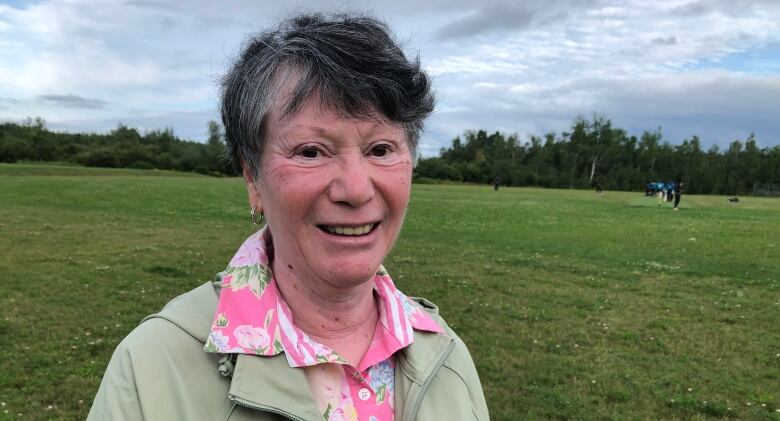 Grey-haired woman with a green sports field behind her. 