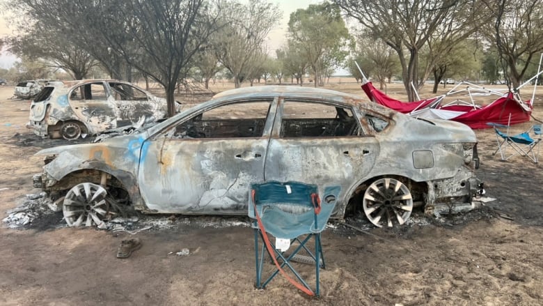 A burned out car with a camping chair in front.