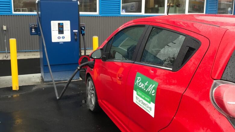 A small red car plugged into an electric vehicle charging station.