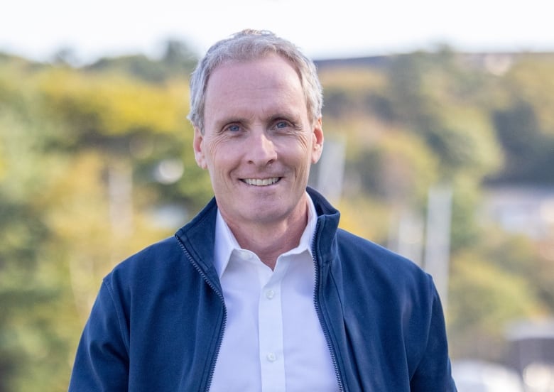 A man in a white shirt and blue unzipped jacket.