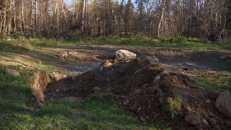 An empty lot where a house once stood. There is green grass, dirt and gravel rocks. 