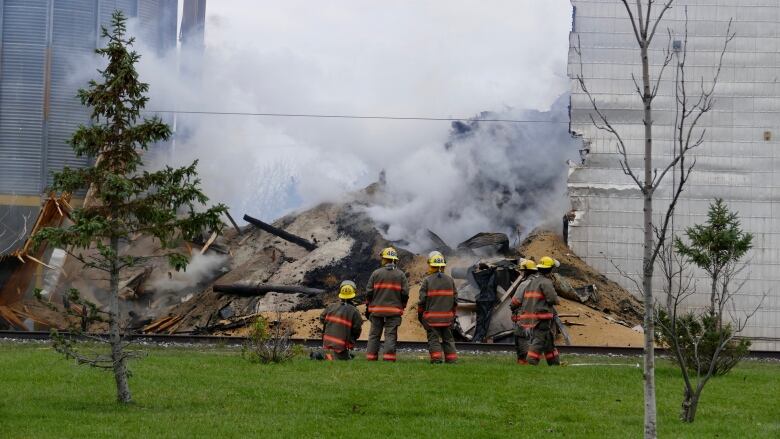 Firefighters stand outside a pile of grain and rubble.