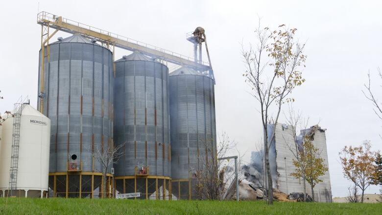 three large steel bins stand next to a burnt building.