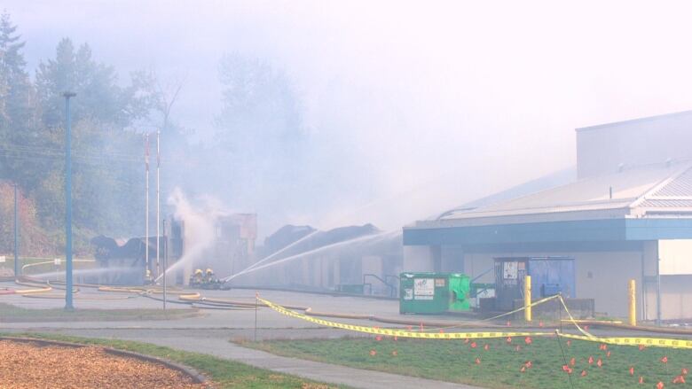 A school with firefighters spraying water on it, heavy smoke in the air and parts of the building crumbling.