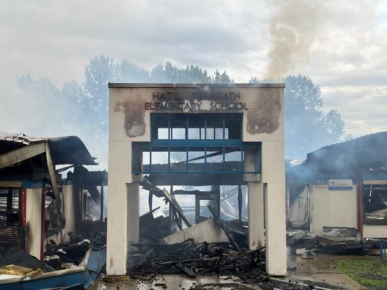 A school entrance stands among the smouldering, smoking ruins of a fire.