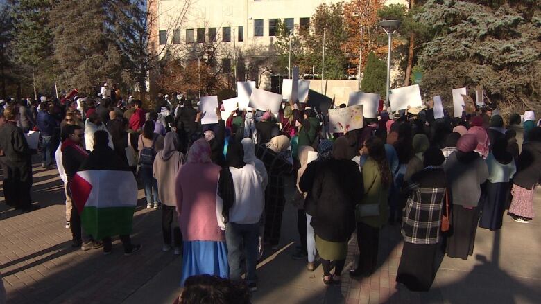 About 100 people are gathered outside Saskatoon City Hall holding up protest signs 