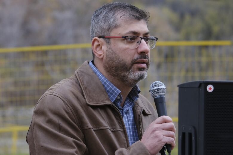 Ahmad Al-Dissi is holding a microphone and has glasses on