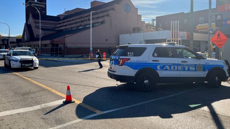 Police and cadet vehicles block a street beside a Shell gas station. Yellow police tape is also strung across the area