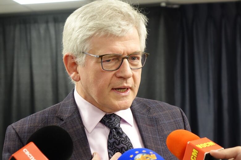 A man with grey hair speaks with microphones in front of him.