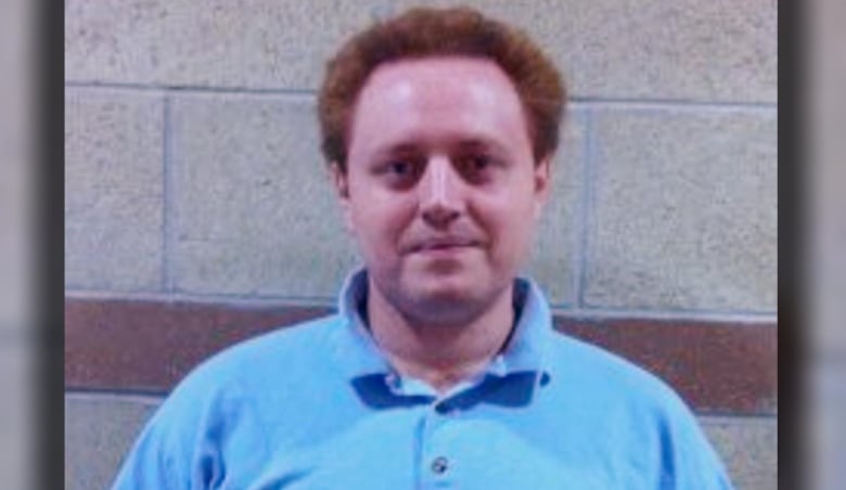 A man in a blue polo shirt poses against a concrete wall.