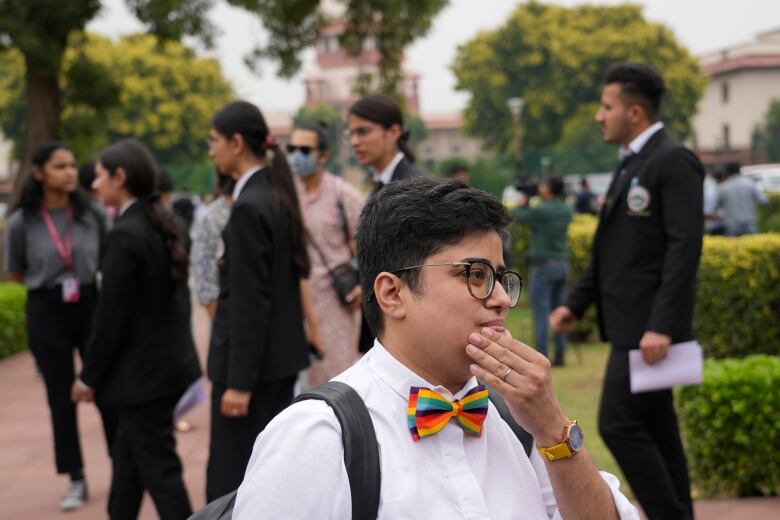 A person in a white collared shirt and rainbow bowtie stands outside a courthouse.