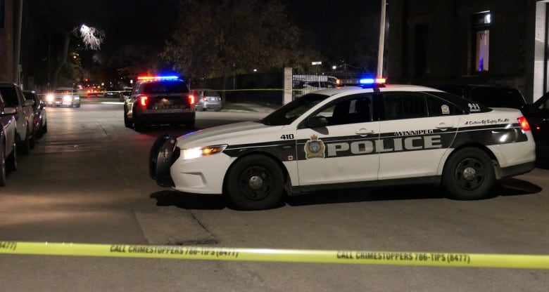 Three police cars and yellow tape block a street at night time.