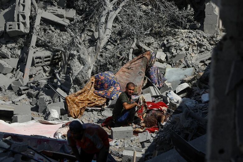 A man reacts next to a body of a woman killed in Israeli strikes on houses, in Rafah, in southern Gaza Strip. He is surrounded by grey rubble.