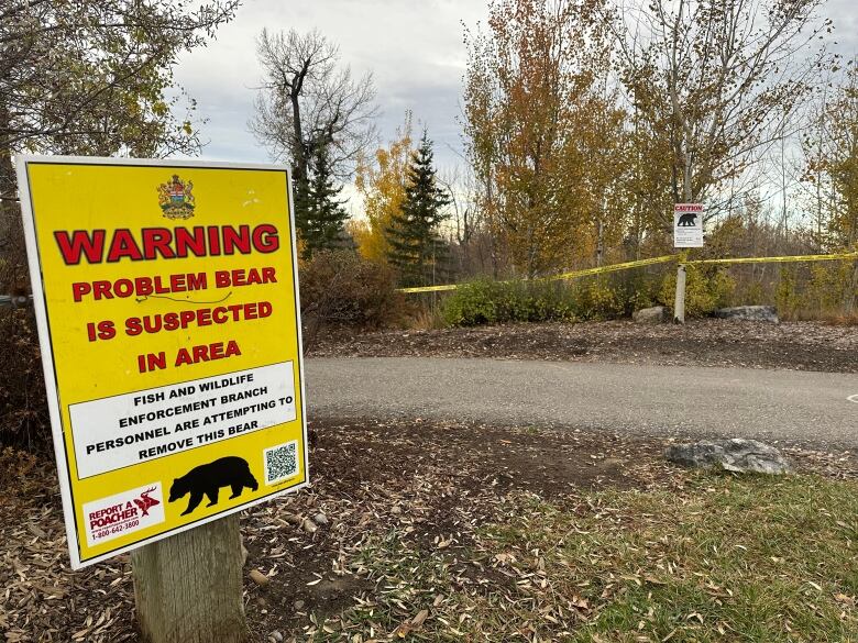 a red and yellow sign outside in a wooded area warns about the presence of a bear