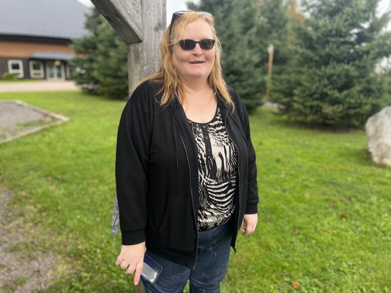 Nancy Riley with a black sweater and sunglasses, standing outside under a pergola.