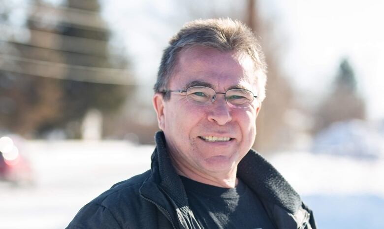 Les Wright, a man with white hair and glasses, wears a black jacket outside.