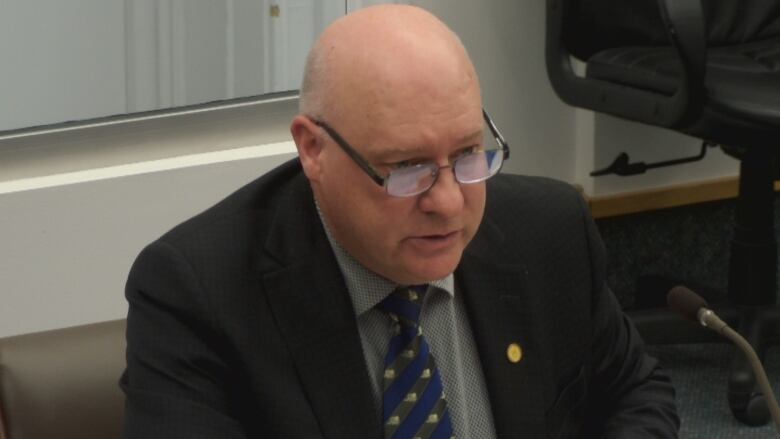 Balding man in glasses and business suit talks into a microphone. 