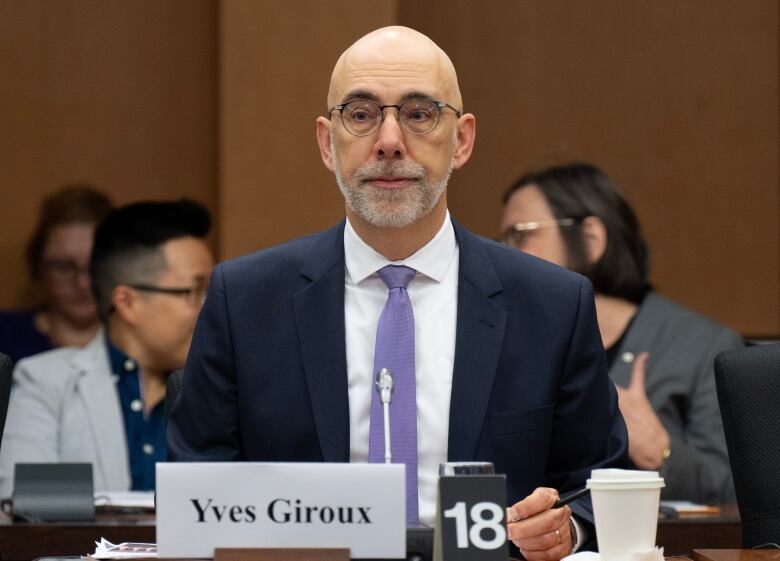 A man in a suit sits in a committee room.