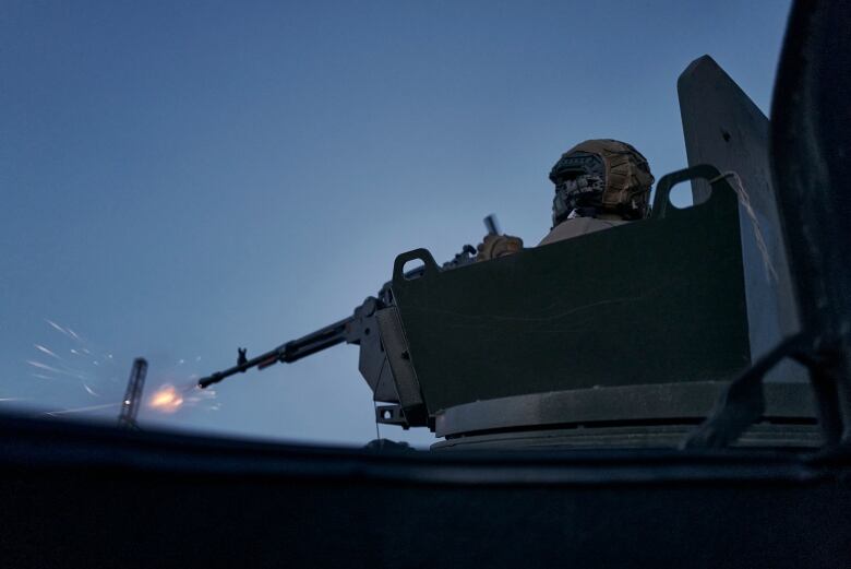 A soldier fires a gun from atop a military vehicle.