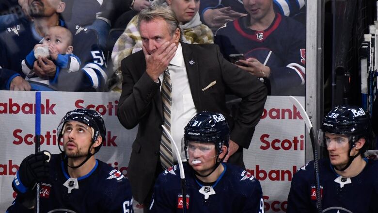 The coach of a hockey team stands behind players who are sitting on a bench.