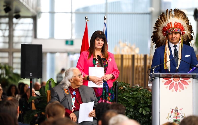 A woman stands on a stage next to a man standing behind a podium.