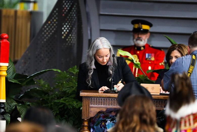 A woman stands at a podium holding a pen.