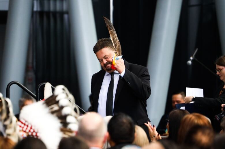 A man wearing a suit and holding a feather stands in front of a crowd of people.