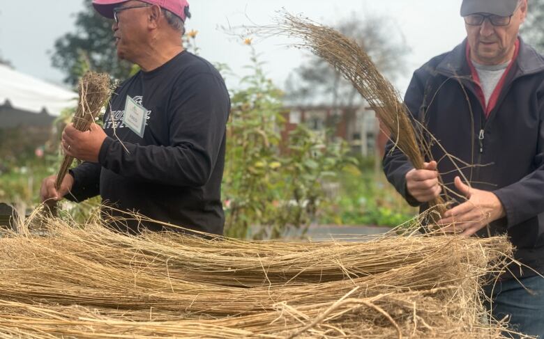 Two men stand behind a pile of dried flax stalks.