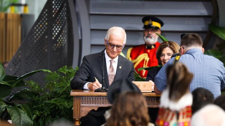  man wearing a suit and tie stands behind a podium holding a pen.