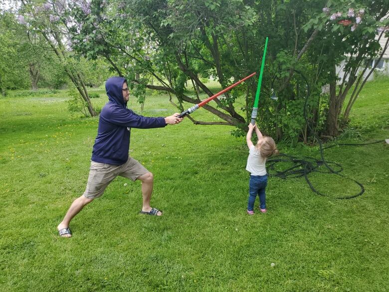 A man and child play with pretend light sabres.