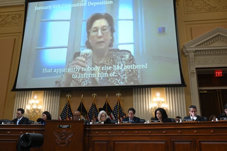 A woman in glasses is shown holding a diet Dr. Pepper can on a video projection above a panel of lawmakers.