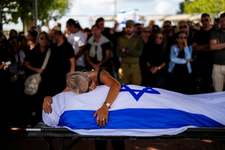 A woman embraces a body covered in an Israeli flag.