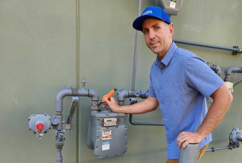 A man in a cap stands near a gas meter.