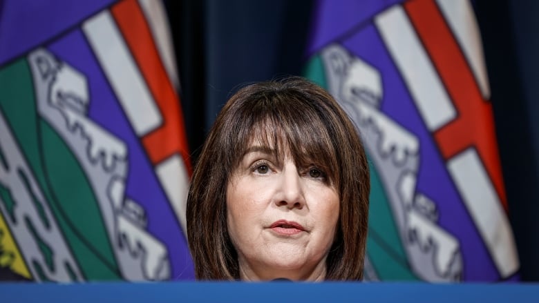 A woman with brown hair with an Alberta flag in the background. 