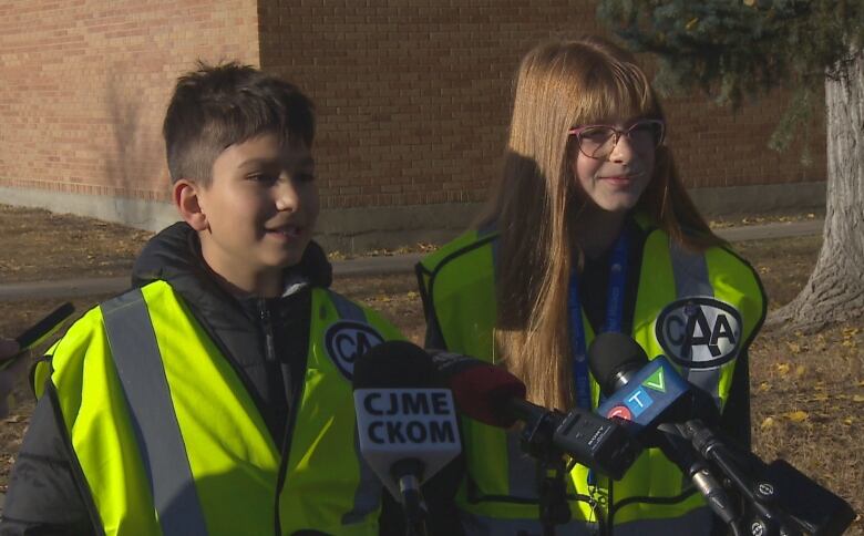 Two kids in yellow safety vests stand in front of microphones.